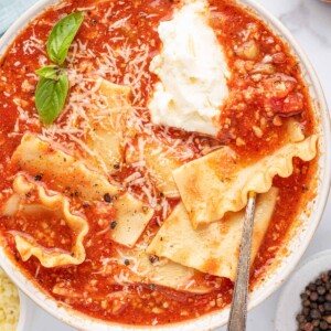 A silver spoon in a bowl of easy lasagna soup with basil leaves, parmesan cheese and a dollop of ricotta cheese.