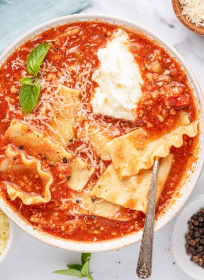 A silver spoon in a bowl of easy lasagna soup with basil leaves, parmesan cheese and a dollop of ricotta cheese.