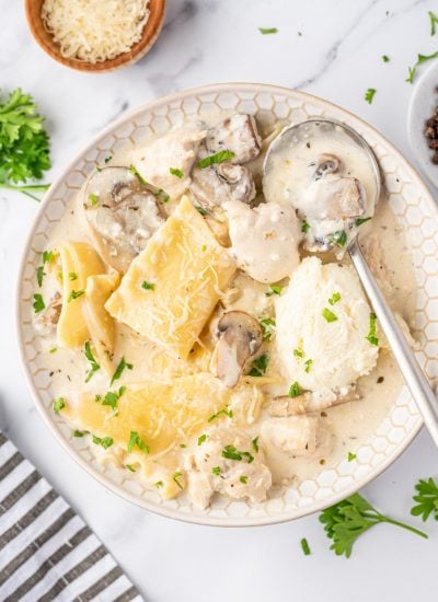 A single serving of creamy white chicken lasagna soup in a bowl with a silver spoon.