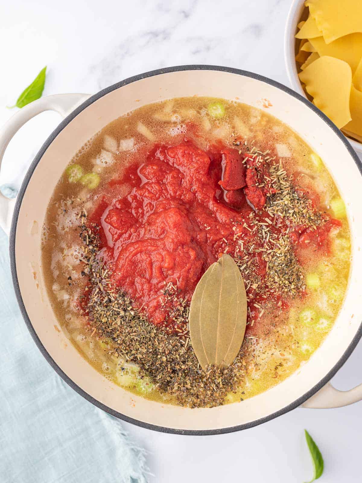 Process photo for making the broth with crushed tomatoes, herbs and spices and a bay leaf.