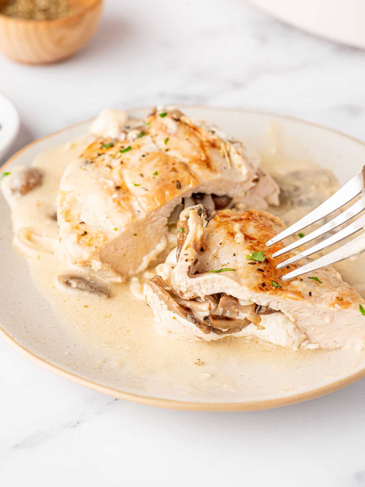 A fork is poised over a bite sized piece of chicken on a plate of mushroom stuffed chicken.