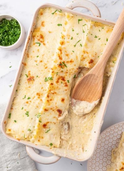 A wooden spoon sits in a casserole dish where several piece of the chicken lasagna recipe have been removed.