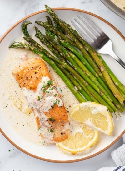 A plate with a fillet of salmon with creamy lemon butter sauce with asparagus and lemon slices.
