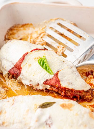 Finished parmesan crusted chicken breasts rests in a baking dish along side a silver spatula.