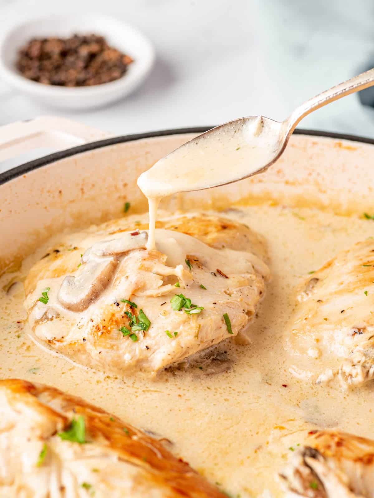 Creamy sauce is dripping off a spoon and onto stuffed chicken breast in a skillet.