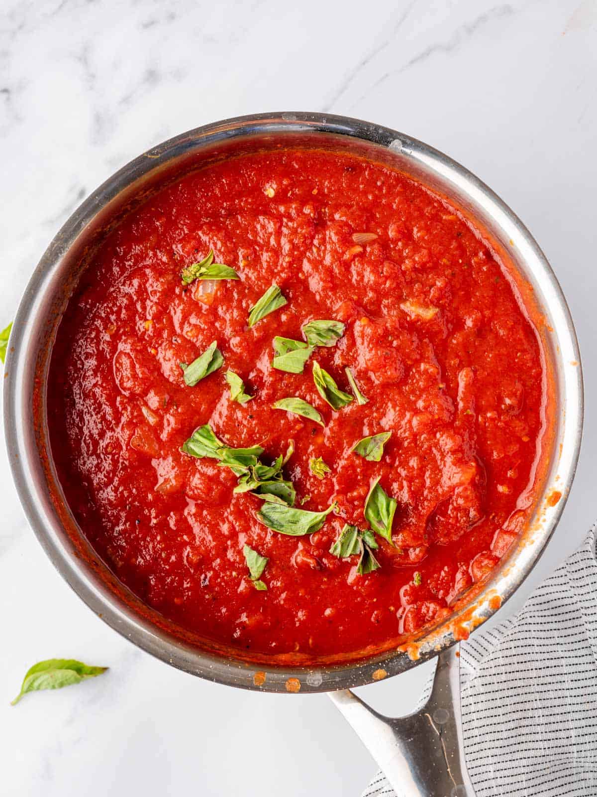 Homemade marinara in a pot topped with chopped basil.