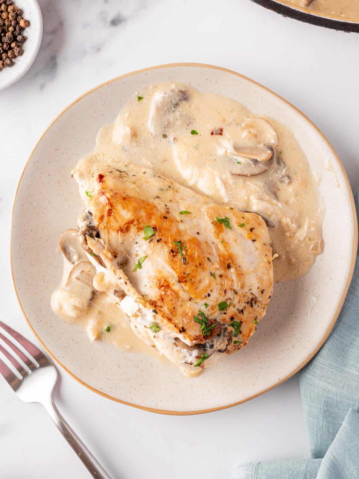 A plate with a mushroom stuffed chicken breast resting on top of the creamy garlic butter sauce. A fork sits to the left.