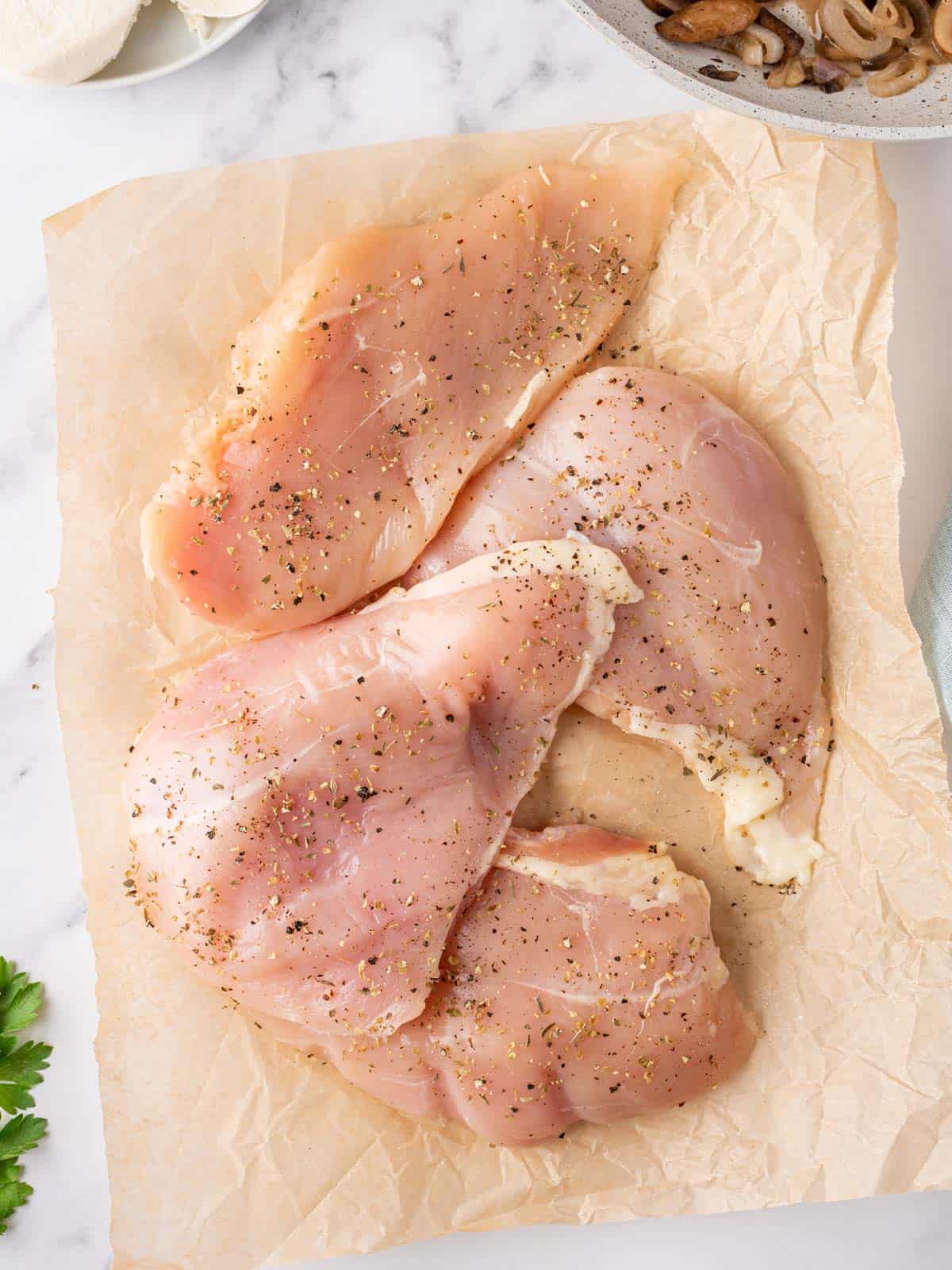 Seasoned chicken breasts on a sheet of parchment paper.