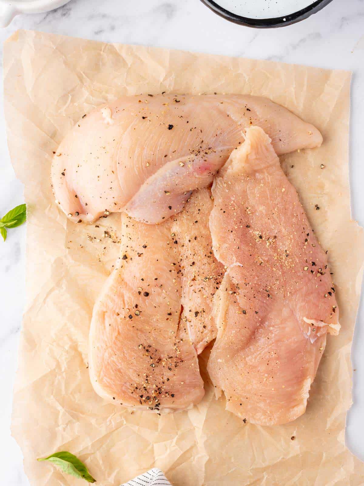 Three seasoned chicken breasts on parchment paper.