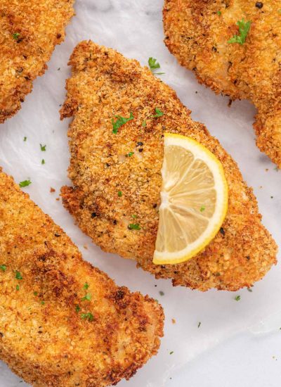 Closeup of a crispy chicken cutlet with a lemon slice on top.