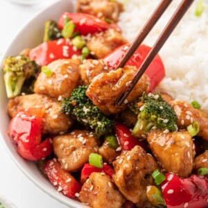 Chopsticks pick up a piece of Chicken Teriyaki Stir Fry from a bowl of rice.