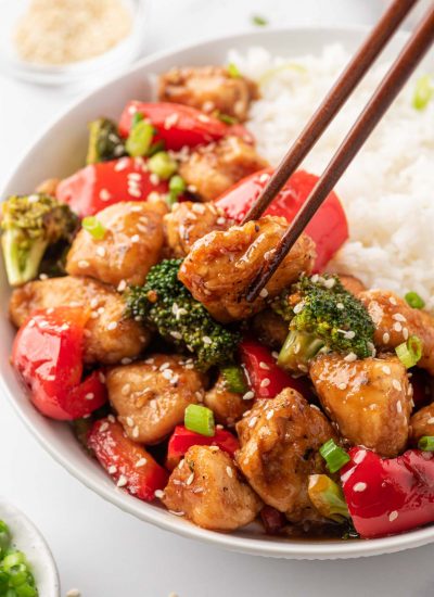 Chopsticks pick up a piece of Chicken Teriyaki Stir Fry from a bowl of rice.