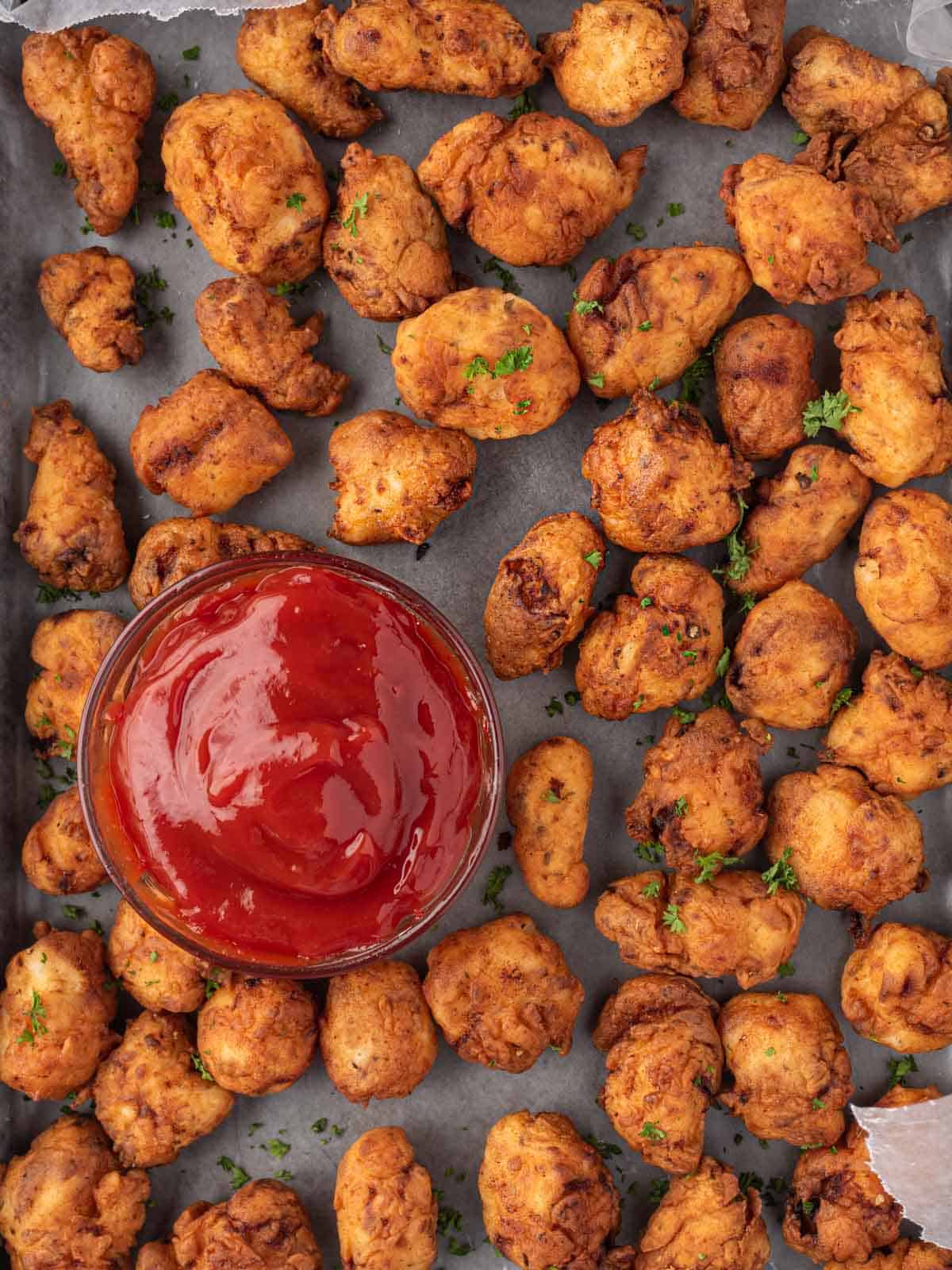 A tray full of homemade popcorn chicken and a bowl of dipping sauce.