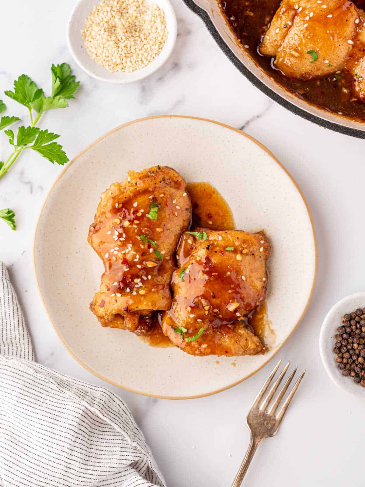 Honey garlic soy chicken thighs on a white plate with a fork beside it.