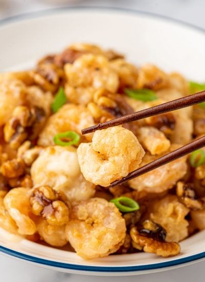 Chopsticks pick up a piece of copycat panda express walnut shrimp from a bowl.