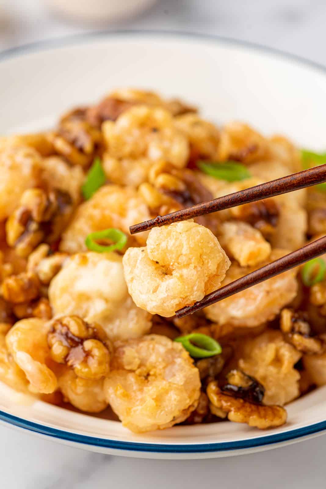 Chopsticks pick up a piece of copycat panda express walnut shrimp from a bowl.