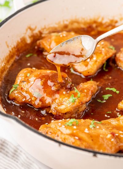 A spoon with a drizzle of honey garlic sauce over a chicken thigh,