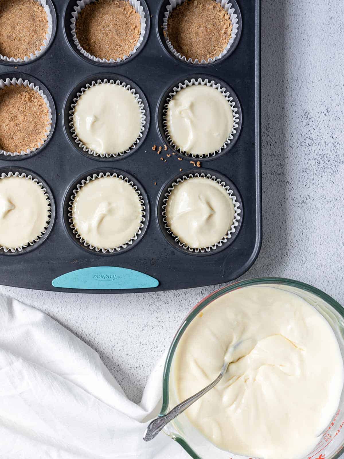 mini cupcake tin being filled with cheesecake filling.