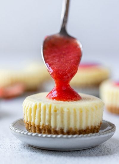spoon topping strawberry sauce onto the mini cheesecake