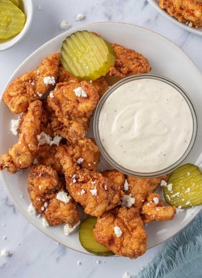 A plate of Nashville hot chicken tenders with pickles and dipping sauce.