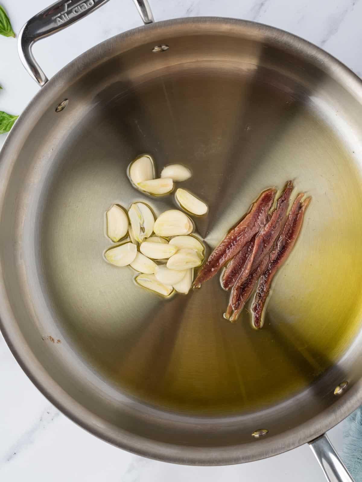Garlic and anchovies added to oil in a pan.
