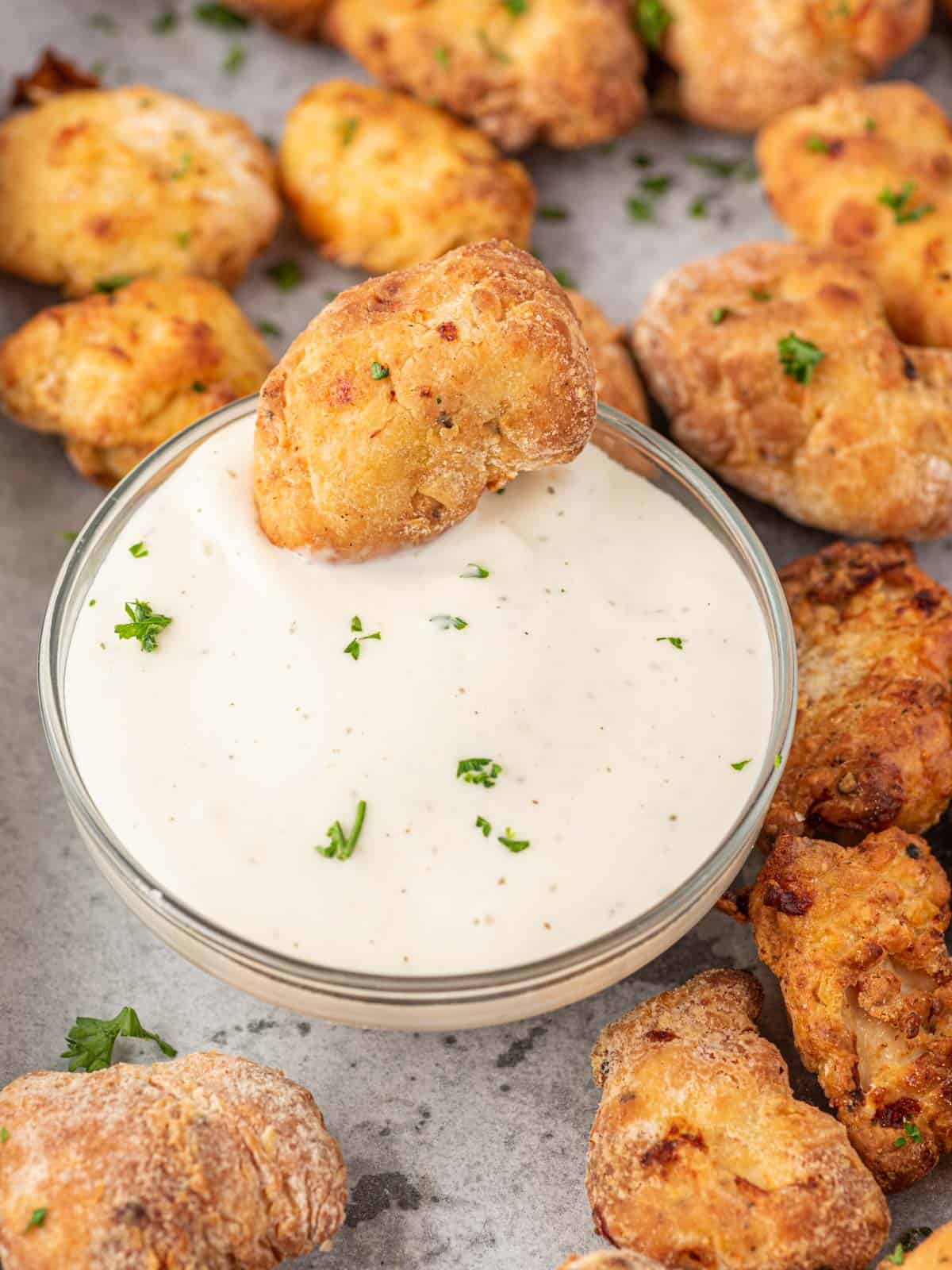 Air fryer chicken nuggets on a tray and one is resting in a bowl of dip.