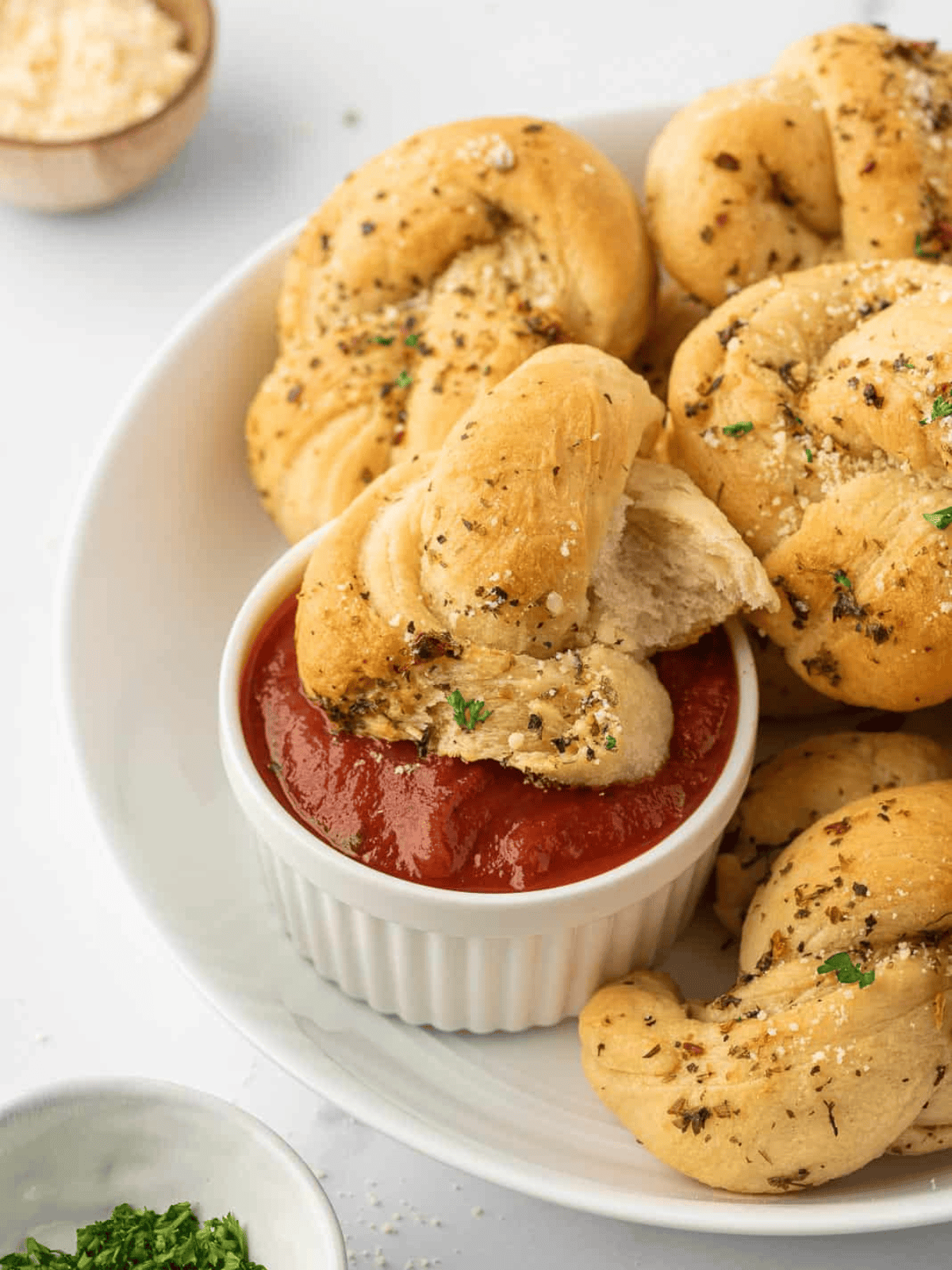 A soft bread knot dipped into a bowl of marinara sauce.