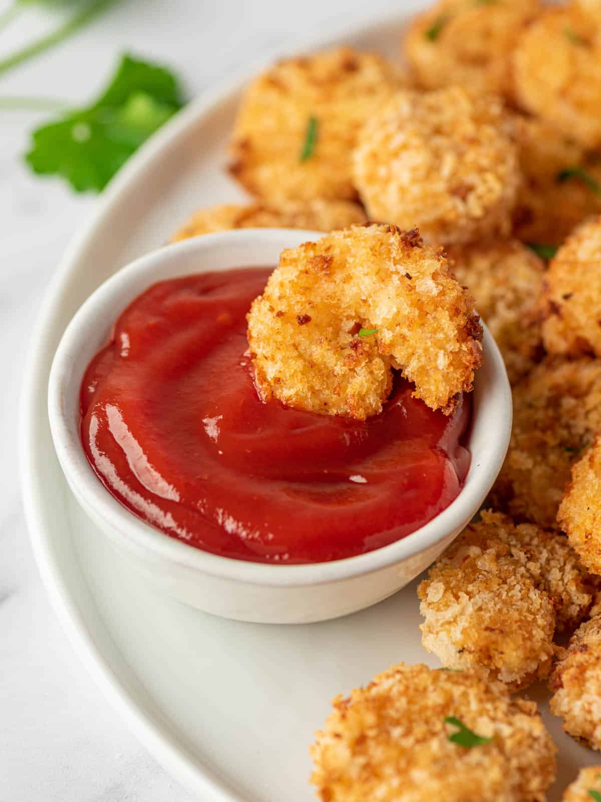 A piece of air fryer popcorn shrimp is laying in a bowl of cocktail sauce.
