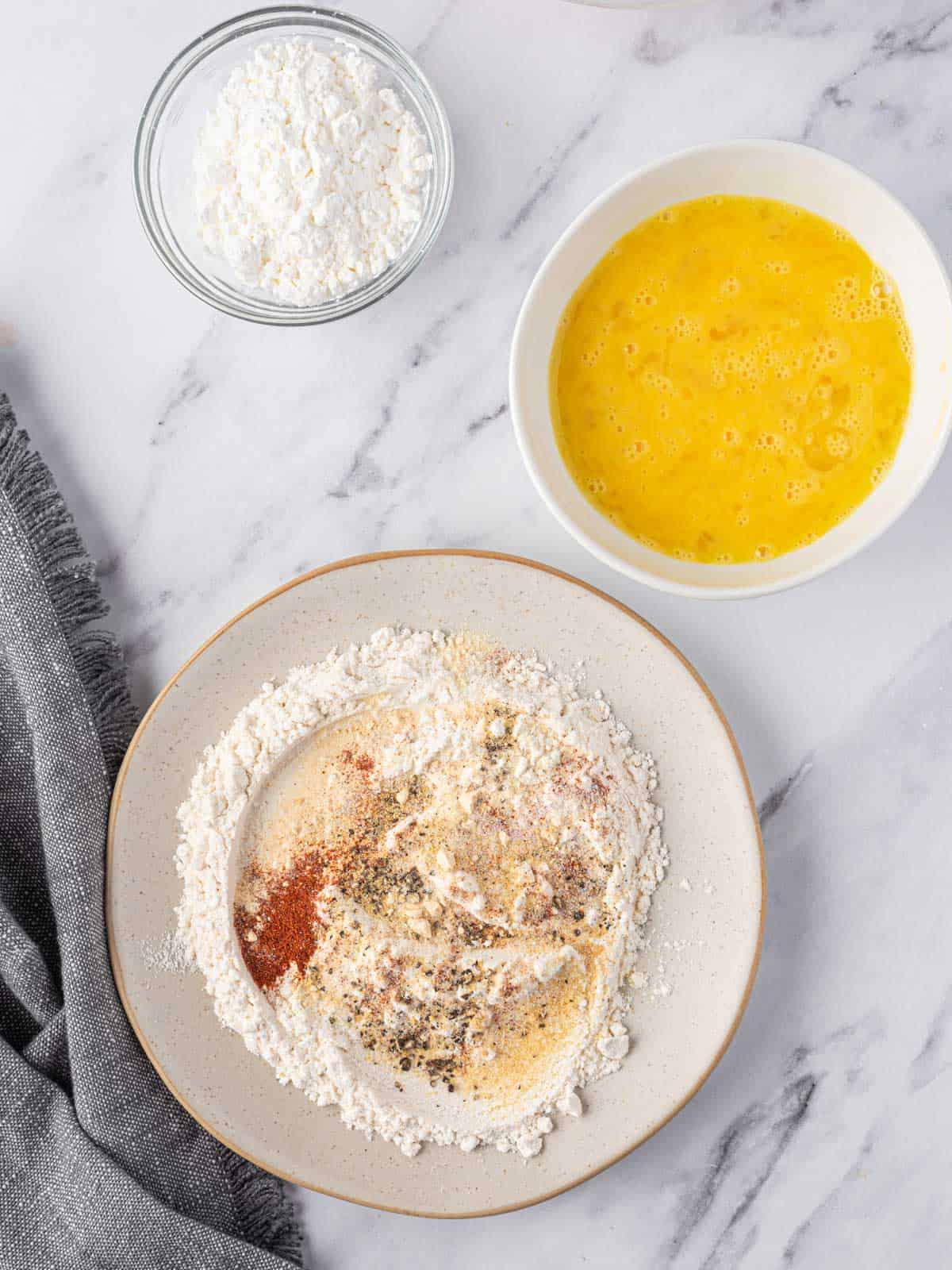 Bowls of seasoned flour, egg and cornstarch for dredging chicken nuggets.