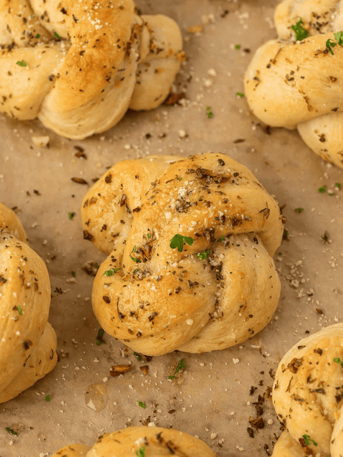 Golden garlic knots brushed with herb butter and sprinkled with parmesan and fresh parsley.