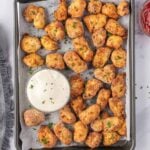 Golden chicken nuggets garnished with parsley and served on a baking sheet with ranch dipping sauce.