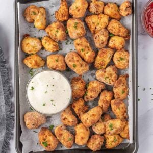 Golden chicken nuggets garnished with parsley and served on a baking sheet with ranch dipping sauce.