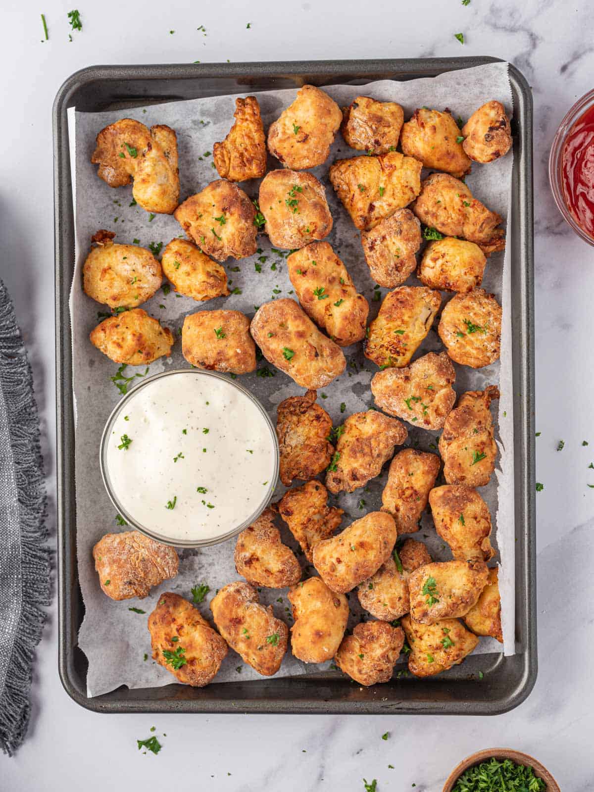 Air fryer chicken nuggets on a parchment lined tray with a bowl of dip.