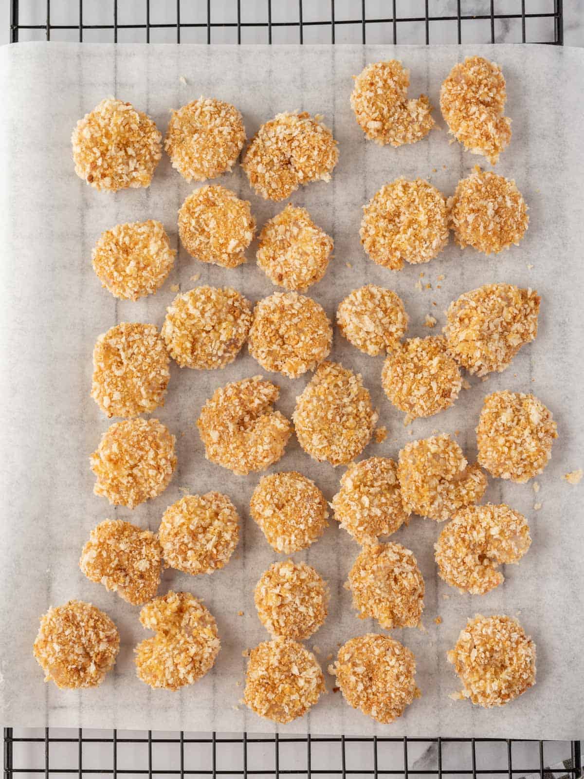 Homemade popcorn shrimp breaded and laying on a baking rack topped with parchment.