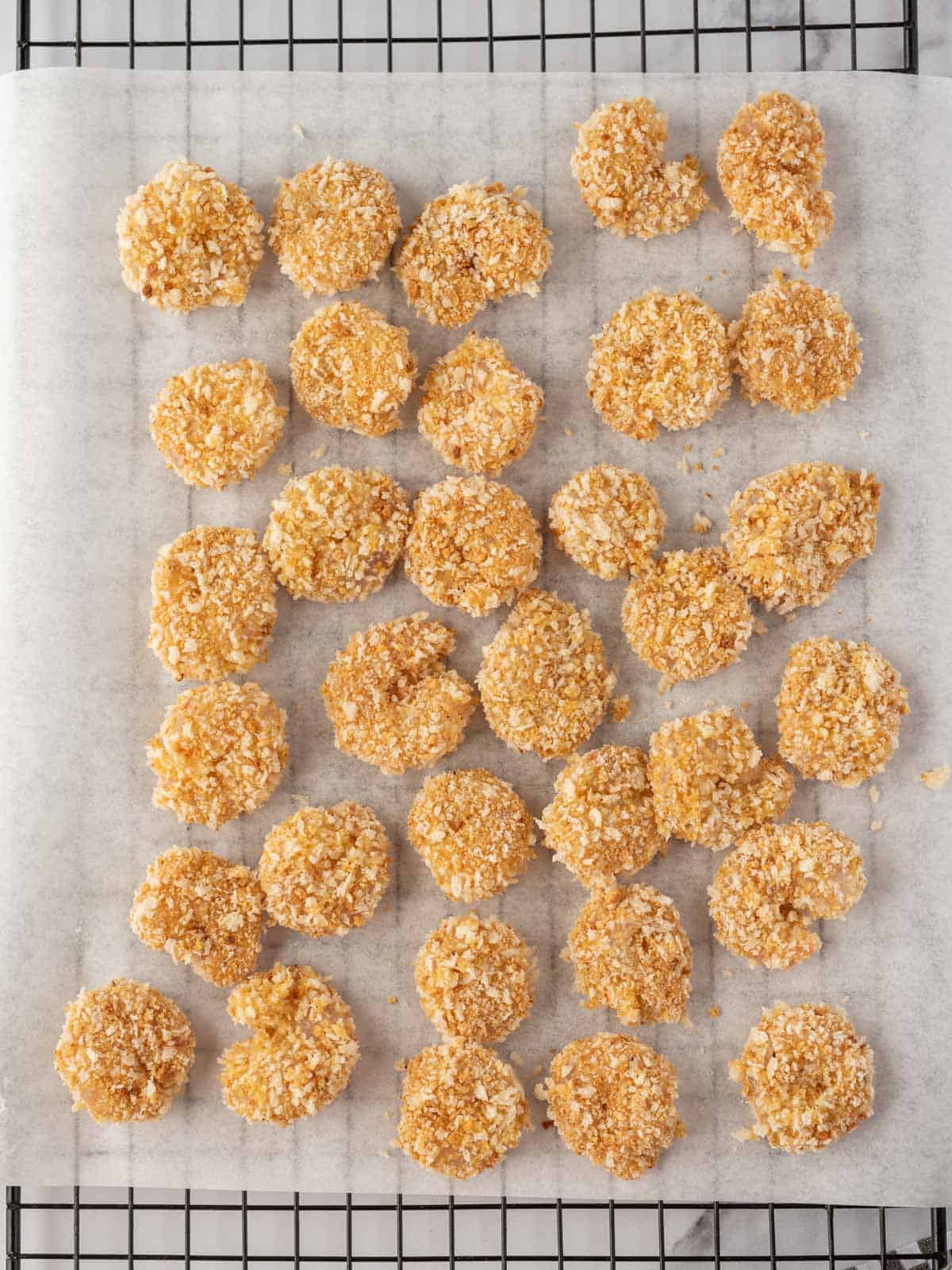 Homemade popcorn shrimp breaded and laying on a baking rack topped with parchment.