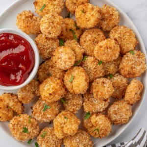 A white tray of air fryer popcorn shrimp with a small bowl of cocktail sauce.