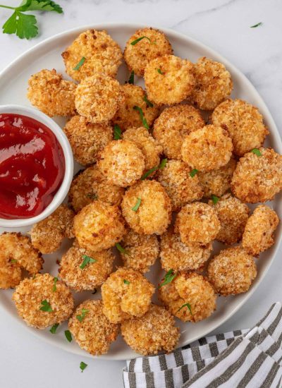 A white tray of air fryer popcorn shrimp with a small bowl of cocktail sauce.