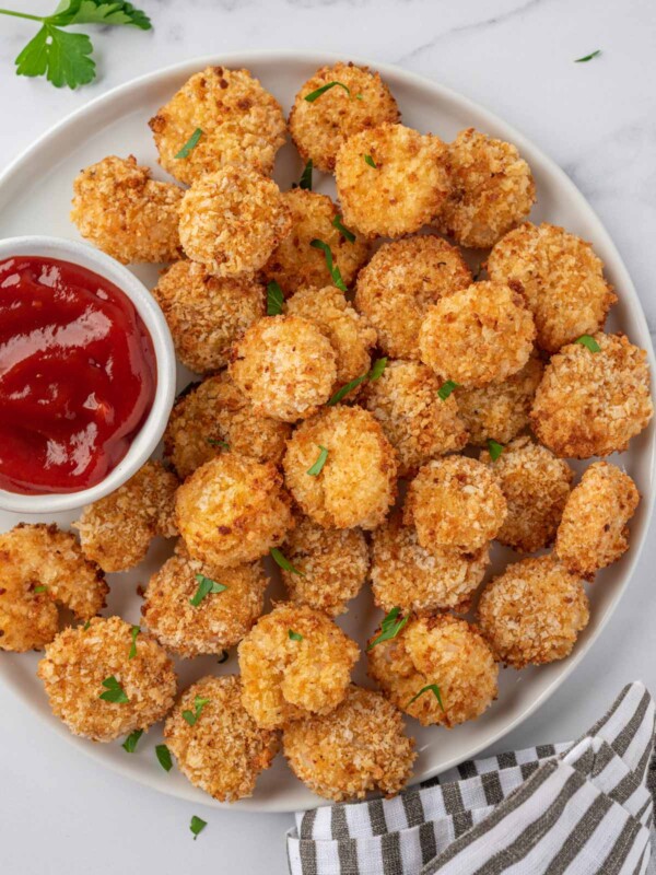 A white tray of air fryer popcorn shrimp with a small bowl of cocktail sauce.