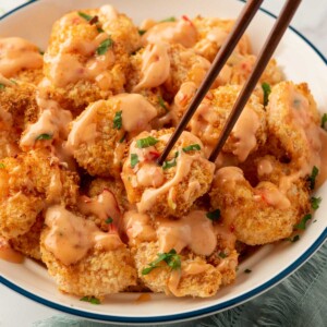 Bang-bang shrimp air fryer on a plate with chopsticks and bang bang sauce.