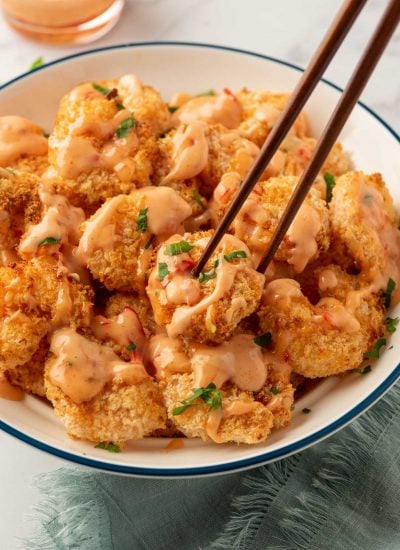 Bang-bang shrimp air fryer on a plate with chopsticks and bang bang sauce.