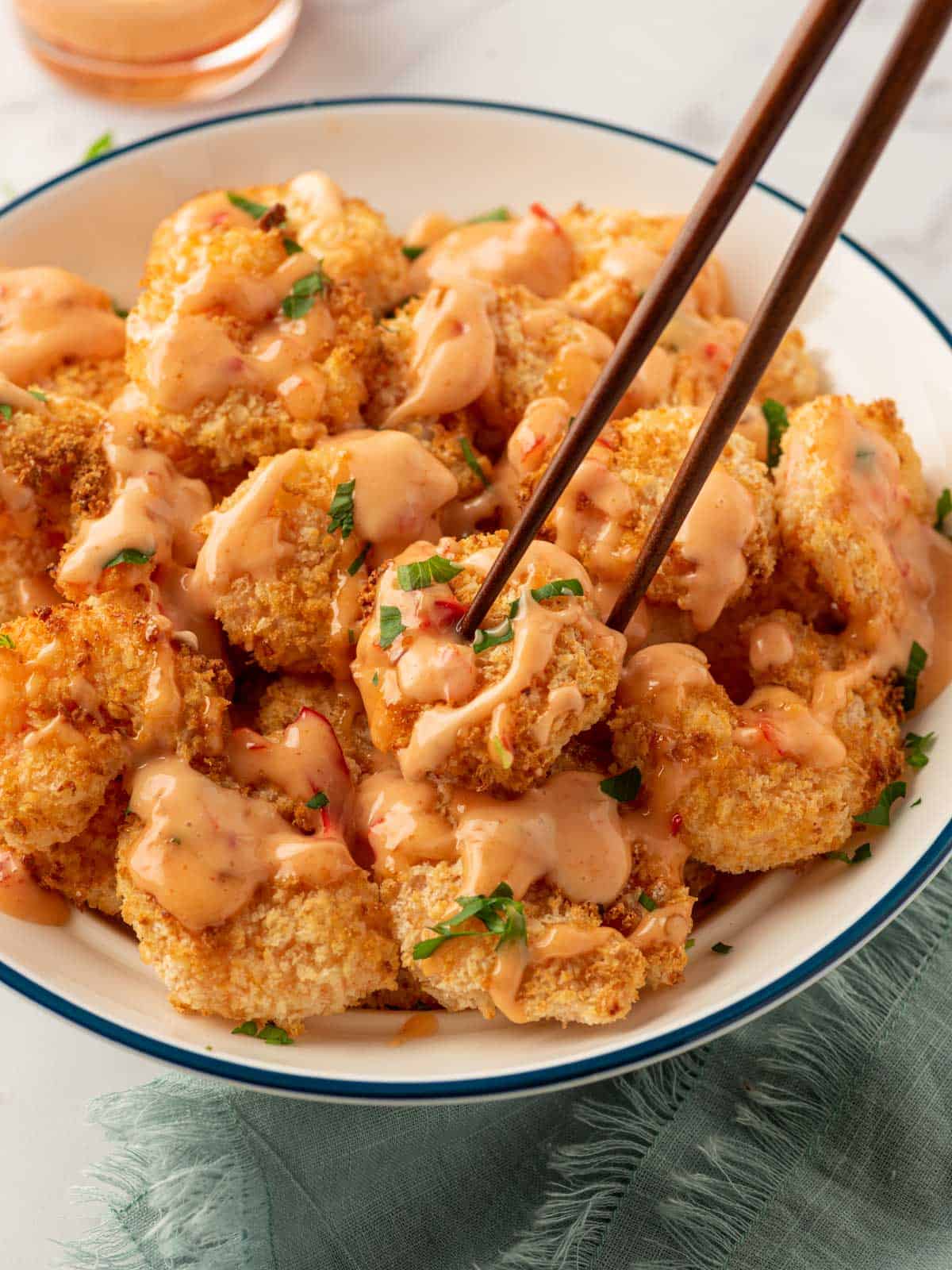 Bang-bang shrimp air fryer on a plate with chopsticks and bang bang sauce.