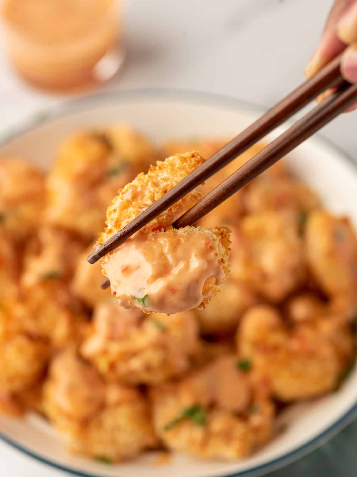 A piece of crunchy air fryer bang bang shrimp being held by chopsticks.