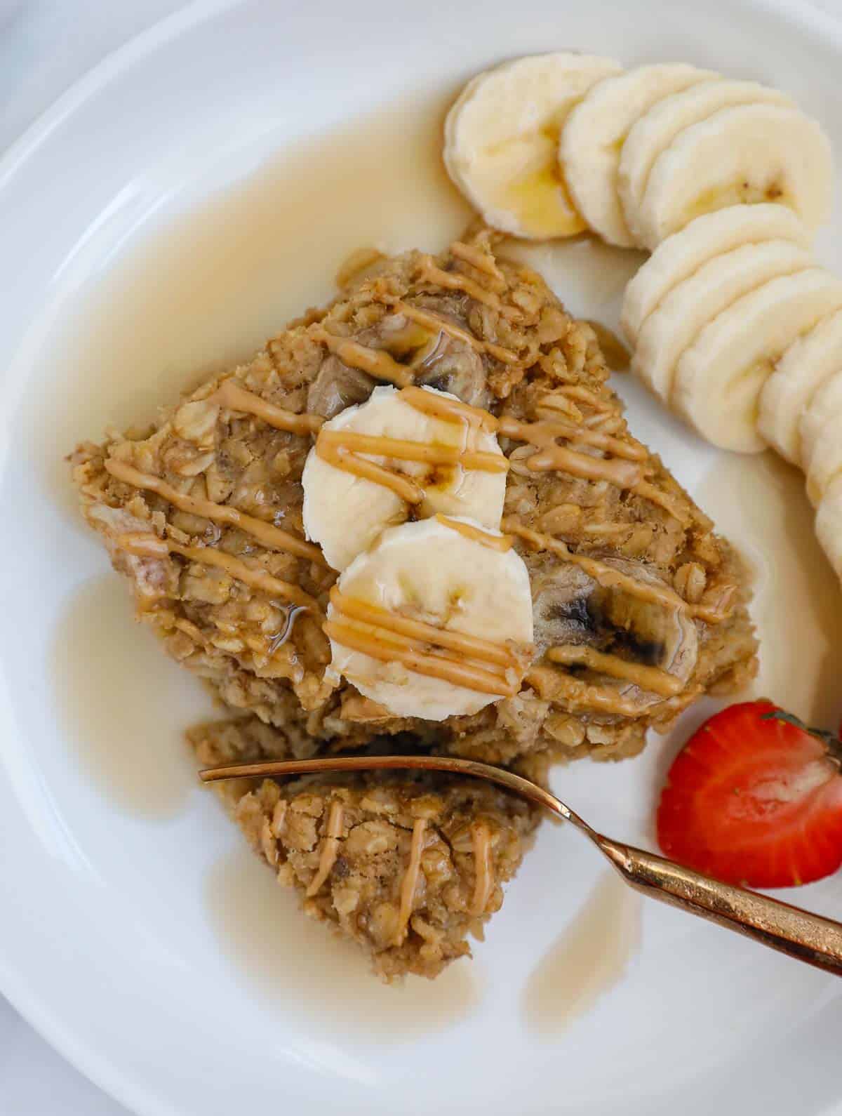 Baked peanut butter banana oatmeal on a plate with bananas and a fork.