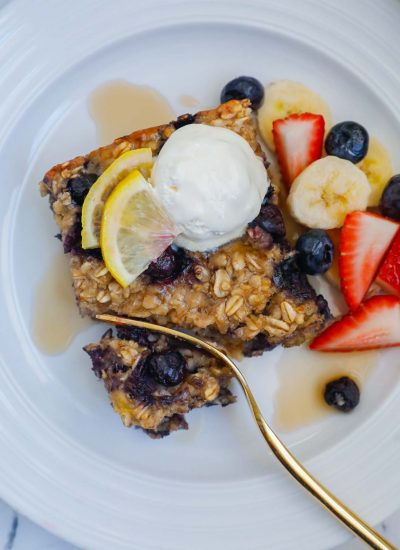 A square of blueberry oatmeal bake on a plate topped with whipped cream and fresh fruit.