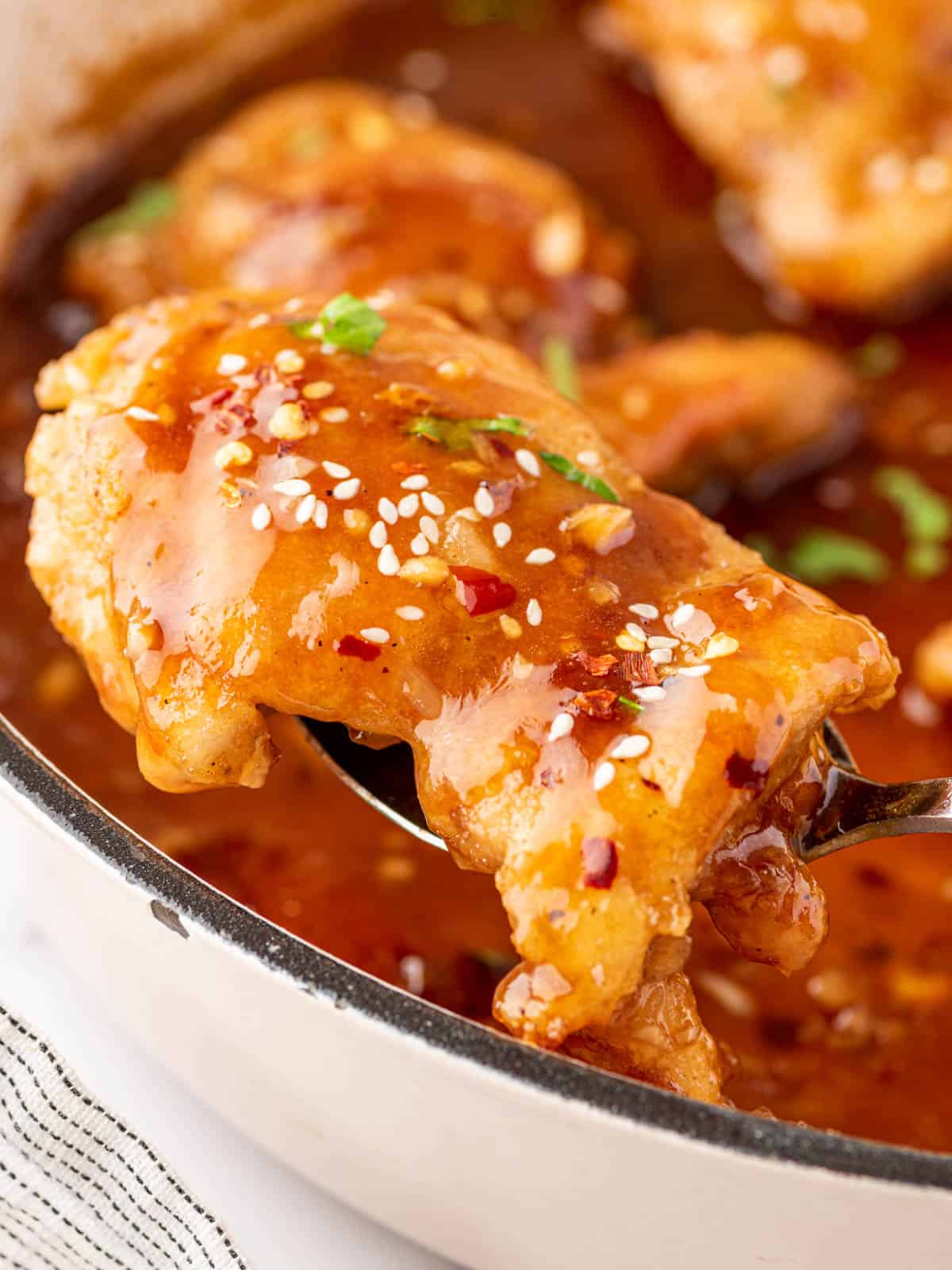 A honey garlic chicken thigh lifted with a spoon.