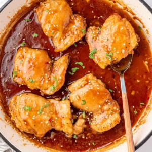 A pan of honey garlic chicken with a spoon under a chicken.