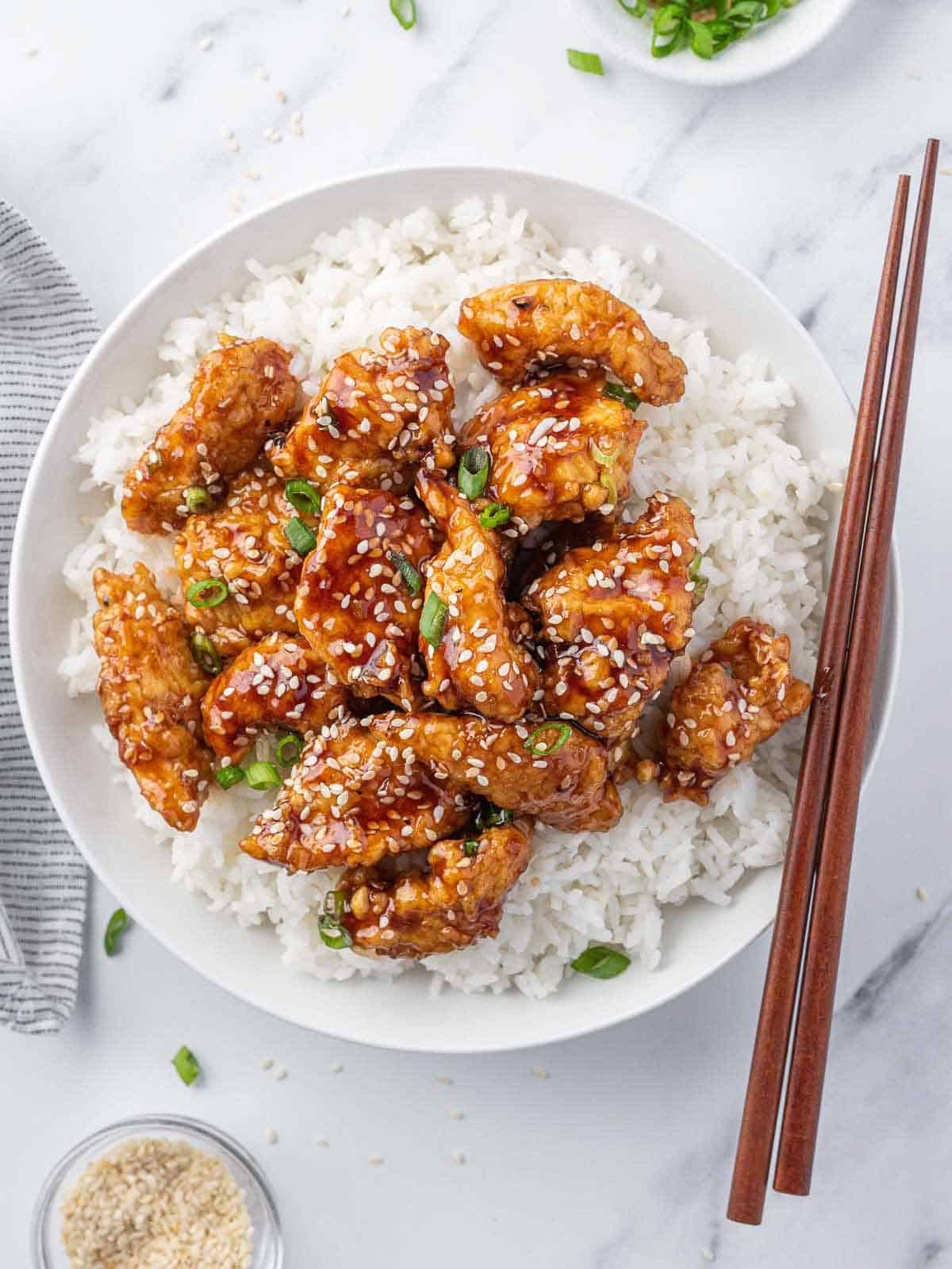 A plate of honey sesame chicken with chopstick resting on the edge.