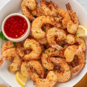 A pile of coconut air fryer shrimp on a plate with dipping sauce.