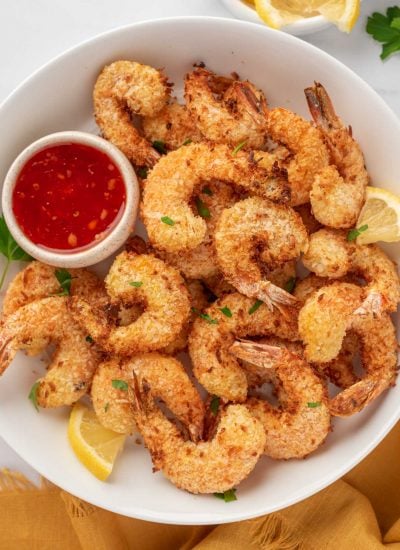 A pile of coconut air fryer shrimp on a plate with dipping sauce.