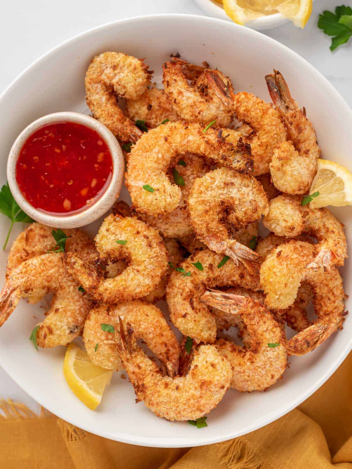 A pile of coconut air fryer shrimp on a plate with dipping sauce.